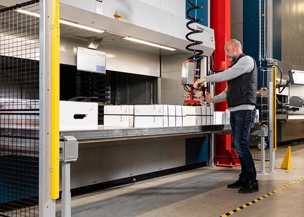 En man som står på ett lager och arbetar med en hissautomat av typen Compact. Detta händer på ett lager.